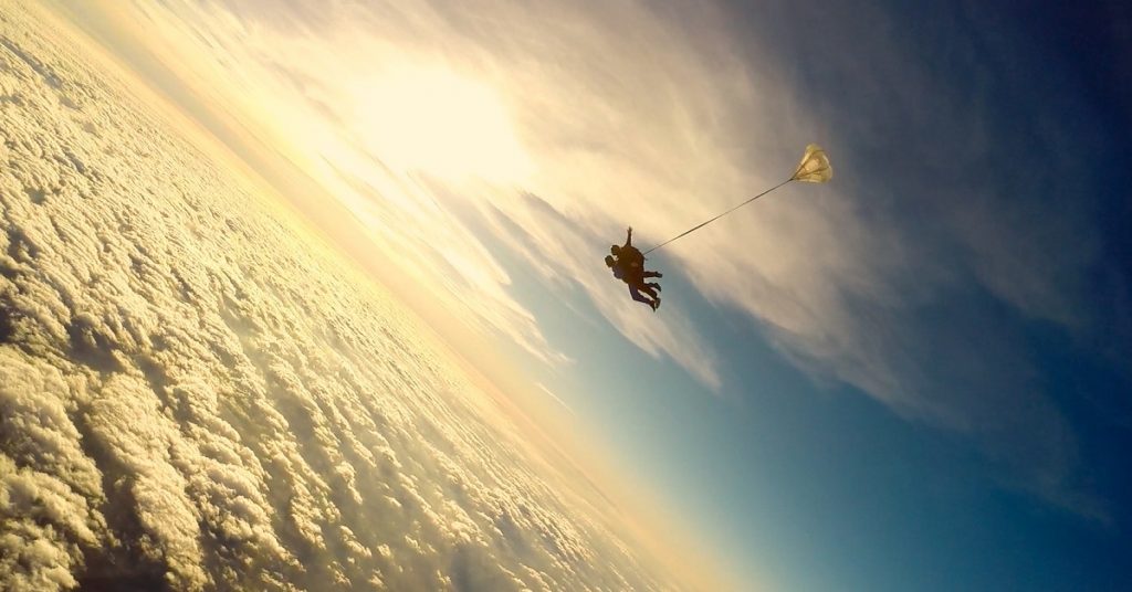 A sillhouette of 2 people tandem skydiving