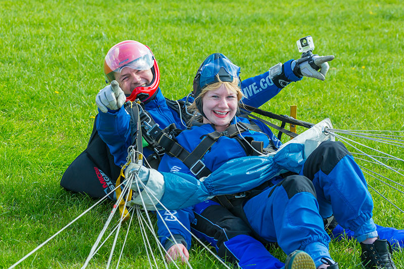 Skydive instructor pointing and smiling at camera with smiling customer having safely landed