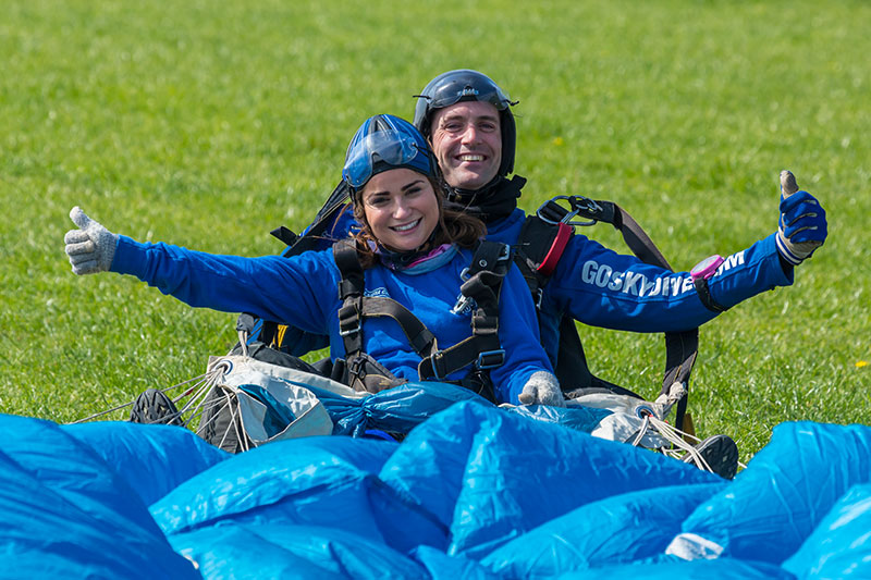 Skydivers smiling with thumbs up after landing.